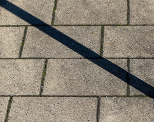 Long shadow stretches across gray pavement as sunlight brightens the urban landscape on a clear afternoon in the city
