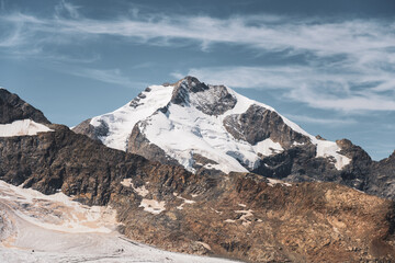 Obraz premium Piz Bernina towers in the Swiss Alps, showcasing its majestic glacier-covered summit against a clear blue sky. The rugged terrain and stunning natural beauty draw visitors year-round.