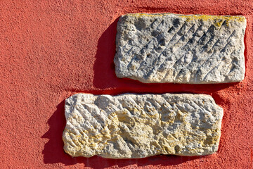 Historic carvings on ancient stones against a vivid red wall reveal stories of the past in an outdoor setting