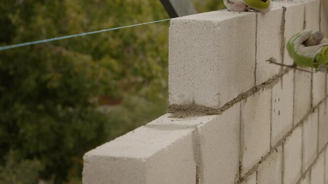 A skilled worker meticulously lays concrete bricks to build a sturdy wall for a new home. The focus is on craftsmanship and careful attention to detail.