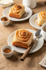 Freshly baked cinnabon roll buns served on ceramic plates with coffee on brown textured background. Cozy autumn menu concept