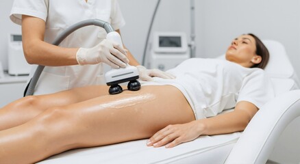 Woman receiving body contouring treatment on her leg. Cosmetologist performing massage therapy with an advanced aesthetic device for skin care.