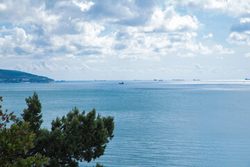 Green hills decorated with rich vegetation, against a gloomy sky full of clouds, convey the essence of the tranquility of nature and the change of seasons, cargo and pleasure ships are visible in the