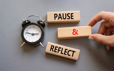 Pause and Reflect symbol. Concept words Pause and Reflect on wooden blocks. Businessman hand. Beautiful grey background with alarm clock. Business and Pause and Reflect concept. Copy space.