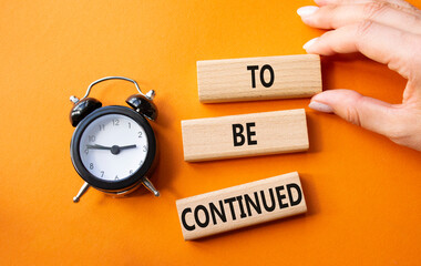 To be continued symbol. Concept words To be continued on wooden blocks. Businessman hand. Beautiful orange background with alarm clock. Business concept and To be continued. Copy space.