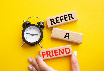 Refer a Friend symbol. Concept words Refer a Friend on wooden blocks. Businessman hand. Beautiful yellow background with alarm clock. Business and Refer a Friend concept. Copy space.