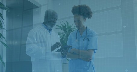 Doctor in lab coat and nurse in scrubs consulting records on tablet in corridor, with stethoscope