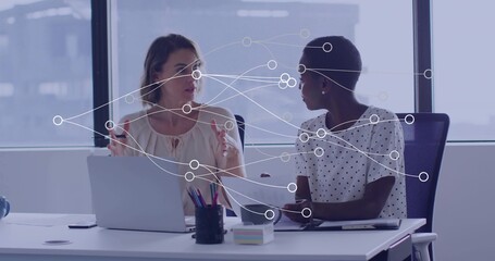 Women in business attire discussing documents in modern office, with network overlay and laptop
