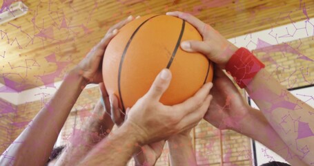 Clustering jersey-clad teammates placing hands around orange basketball in gym, with red wristband