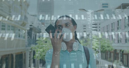 Speaking into smartphone man wearing face mask and headphones on city street, with data overlays