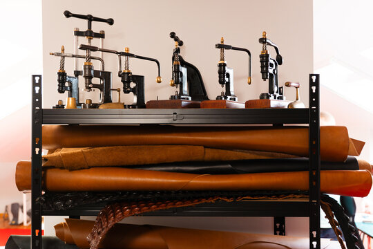 Retro leathercraft presses and shelves of cowhide hides create a true artisan studio. Leather rolls and classic vintage presses fill the craftsman workshop shelves.