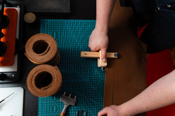 Craftsman preparing leather strap using wooden cutter on mat. Handmade leather belt preparation with wooden strap cutter on cutting mat. Artisan is cutting leather strip with wooden tool.