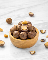 Macadamia nuts with shell in wood bowl with broken macadamia on marble table background