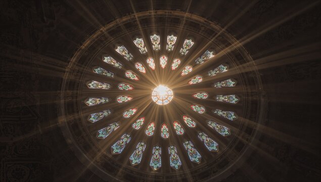 Shining stained glass rosette window casting golden sunbeams inside cathedral nave, carved tracery