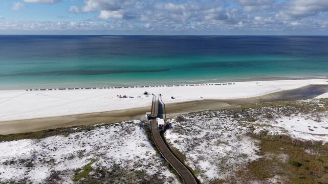 Beautiful drone orbit fly at sandy dunes and turquoise gulf bay with walkway and sunbathers along the shoreline, 30A, Florida, USA
