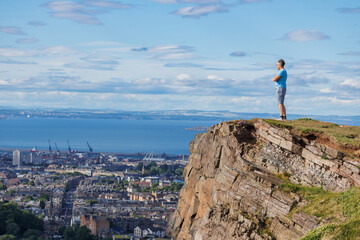 Scenic view of person hiker on cliff by city Edinburg and sea
