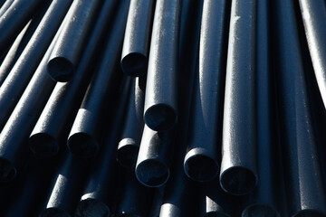 Close-up of stacked black pipes is shown in close-up, highlighting their smooth surfaces and round holes, creating an industrial atmosphere and demonstrating the quality of the material. High quality