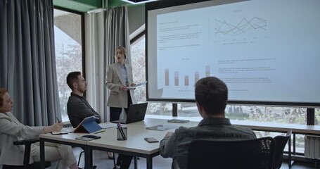 Business team in a meeting room analyzing graphs and charts projected on a screen. A woman leads the presentation, discussing company growth and product performance. - Powered by Adobe