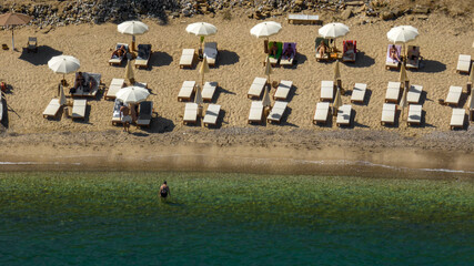 Aerial view of a beach resort with sun loungers and white parasols on a sandy beach. Tourists are holidaying at the beach club.