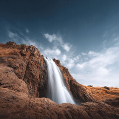 Majestic waterfall cascading down rocky cliffs under a vibrant blue sky. Serene nature scene, perfect for travel, adventure, or environmental concepts. Untamed beauty.