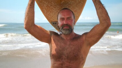 Happy fit senior having fun surfing at sunset time. Sporty bearded old man training with surfboard on the ocean beach. Elderly healthy male lifestyle, extreme sport concept. Active lifestyle, tropical