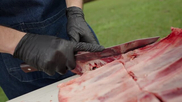 lose-up captures the asador wearing black gloves, slicing through a slab of costillar with a sharp knife, as raw ribs rest on a clean surface, reveals marbling and structure, ready to meet the heat.