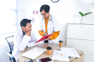 Obraz premium Focused Male Doctors Collaborating on Patient Case Reviewing Medical Charts Together in Bright Clinic Office