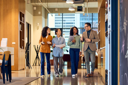 Diverse Group Of Colleagues Walking And Talking In Modern Office Hallway During Break