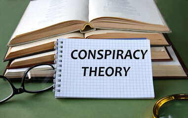 Notebook with CONSPIRACY THEORY text on a green background with books and glasses