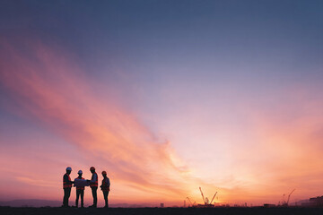 Fototapeta premium Silhouette of engineers reviewing blueprints at sunset. Symbolizes teamwork, construction, and progress. Perfect for project management, architecture, and development.