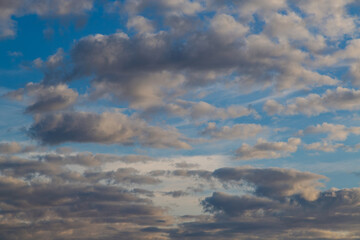 A band of dark gray clouds in the blue sky with reflections of the evening sun and clouds receding into the sunset haze.