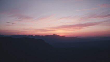 Fototapeta premium Displaying mountain ridges silhouetting under colorful dawn sky, with wispy clouds adding texture