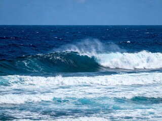 Powerful ocean wave breaking with white foam under clear blue sky