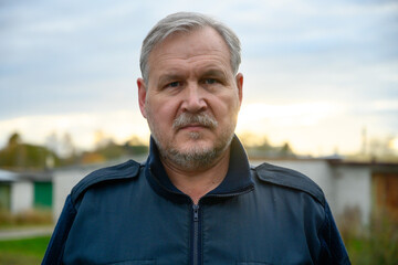 Portrait of mature man with kind eyes and gray beard in backlight at sunset.