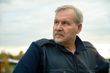 Portrait of mature man with gray beard looking aside in backlight at sunset.