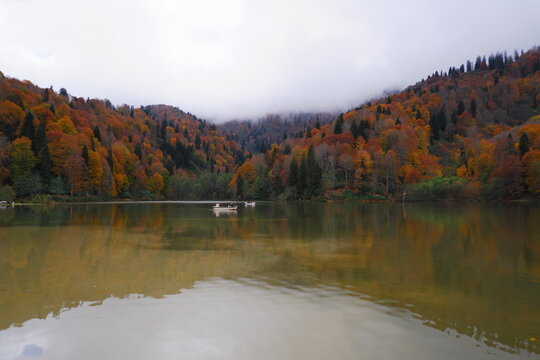 Two small boats on the tranquil surface of a mountain lake, surrounded by a dense forest with vibrant autumn colors