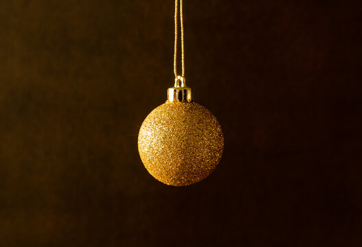 Boule de No&euml;l &agrave; paillettes dor&eacute;es suspendue &agrave; un fil or centr&eacute;e dans l'image, arri&egrave;re plan brun fonc&eacute;