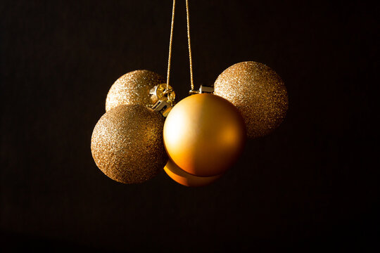 Plusieurs boules de No&euml;l dor&eacute;es scintillantes suspendues  au centre de l'image sur un fond brun fonc&eacute;