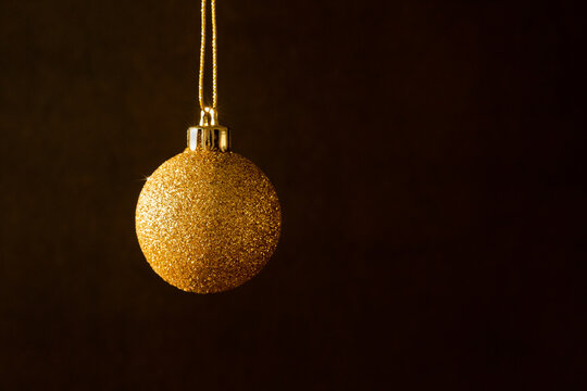 Boule de No&euml;l dor&eacute;e &agrave; paillettes scintillantes suspendue &agrave; un fil or &agrave; gauche de l'image, arri&egrave;re plan brun fonc&eacute;