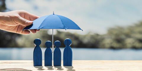 Life insurance and family safety concept with a hand holding a blue umbrella and wooden toys representing family members © guguart