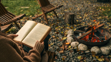Cozy autumn scene with a person reading a book by a crackling fire