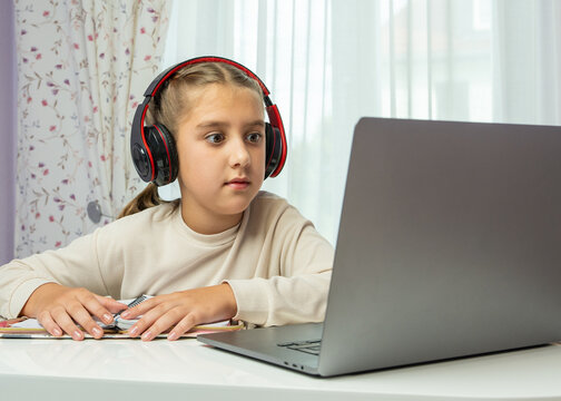 Child wearing headphones focused on laptop screen during home study session. Great for illustrating online education, remote learning, technology in modern childhood.