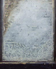 Close-up of weathered and partially erased text on a glass surface, framed by chipped dark wood. The faded black letters on a cloudy white background evoke age, decay, and forgotten information.