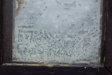 Close-up of weathered and partially erased text on a glass surface, framed by chipped dark wood. The faded black letters on a cloudy white background evoke age, decay, and forgotten information.