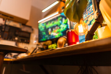 Cozy modern desk setup with warm ambient lighting and green monitor glow, featuring gadgets, keyboard, mic, and gaming chair in a stylish studio workspace. Perfect for background or lifestyle tech the