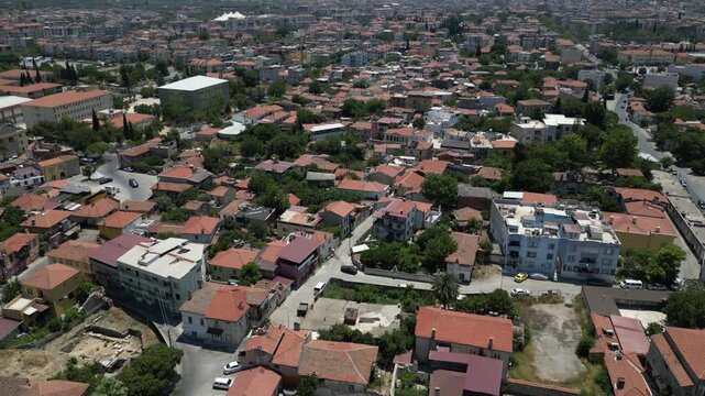 Aerial view of various buildings with red rooftops and green trees interspersed, creating a vibrant contrast of colors and textures, Milas, Mugla, Turkey.