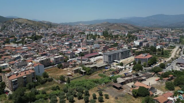 Aerial view of buildings with red roofs contrasting against the lush green trees and distant mountains in the city, Milas, Mugla, Turkey.