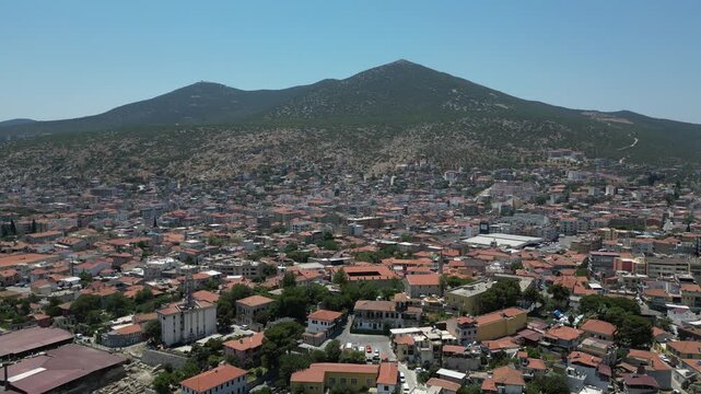 Aerial view of the vibrant cityscape of Milas, where terracotta roofs meet lush green trees against the backdrop of a majestic mountain, Milas, Mugla, Turkey.