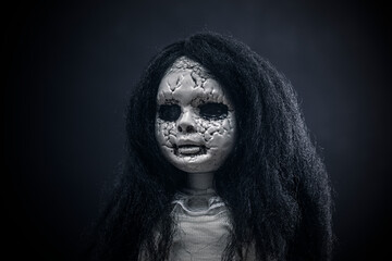 Portrait of a scary cracked doll with black hair on dark background