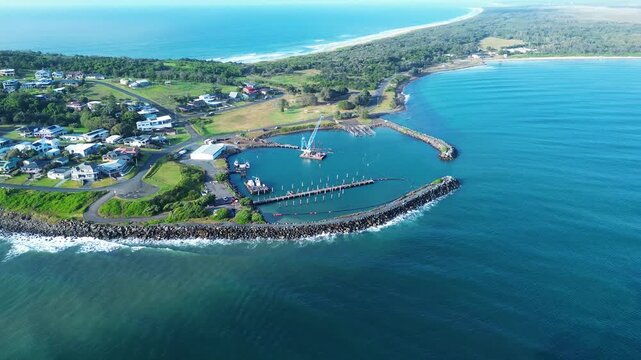 Drone aerial landscape of crane and wharf dock at Crowdy Head Boat Harbour rocky break wall with suburban town housing and bushland beach coastline near Taree Australia industry maritime tourism